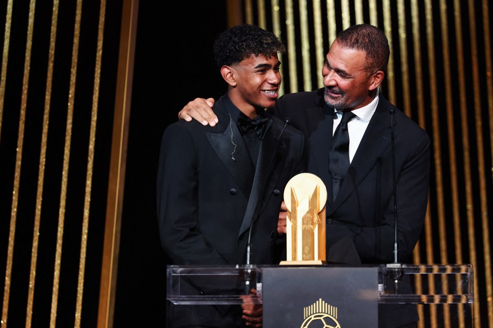 a man in a suit stands next to another man holding a trophy