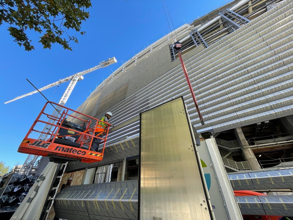 Worker installing metal plates on a stadium facade.