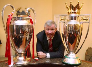 Manchester United manager Alex Ferguson poses alongside the Champions League and Premier League trophies in 2008.