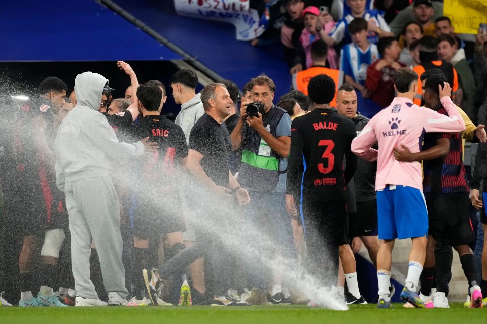 Hansi Flick, Barcelona's head coach, celebrating a victory with his team amidst water sprinklers.